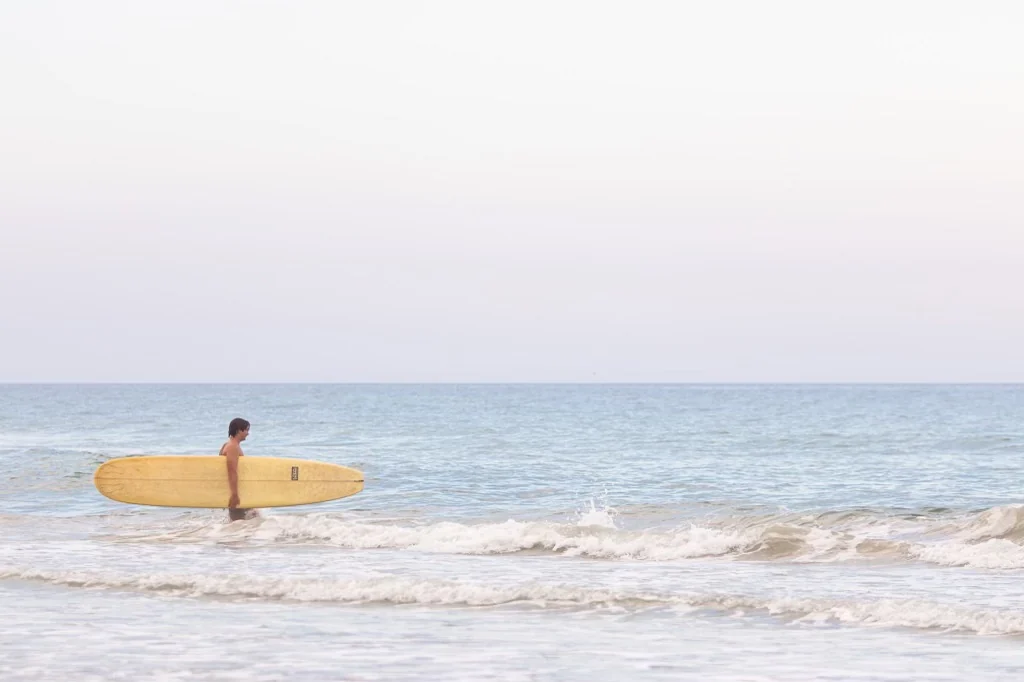 A surfer wading into the water with a longboard at New Smyrna Beach